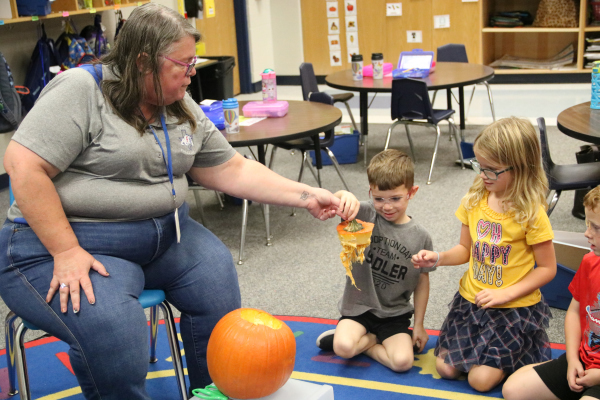 Ms. Morris handing student part of a pumpkin
